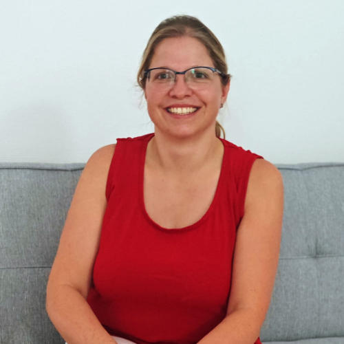 Foto zeigt die examinierte Altenpflegerin Melania Fiorentino, die auf einem Sofa sitzt und freundlich lächelt.